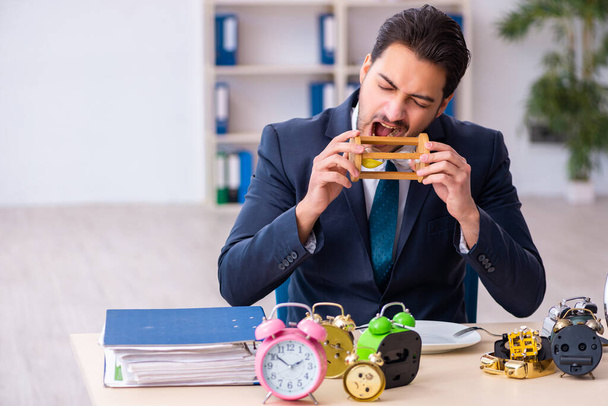 Молодой бизнесмен ест будильник - Фото, изображение