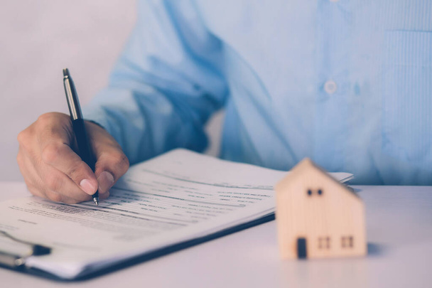 Real estate agent holding home and signing contract about agreement of real property on desk, house broker and planning investment, businessman writing on document form rent house, business concept. - Photo, Image