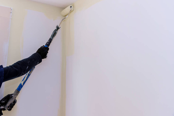 Langstieliger Farbwalzenpinsel mit weißer Grundierung auf Wand bei Hausrenovierung auftragen - Foto, Bild