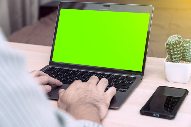 自宅のノートパソコンで働く若いビジネスマン,オフィスの机でノートパソコンを使用して忙しいビジネスマンの手の緑の画面を表示,木製のテーブルに座ってコンピュータを入力します。 - 写真・画像
