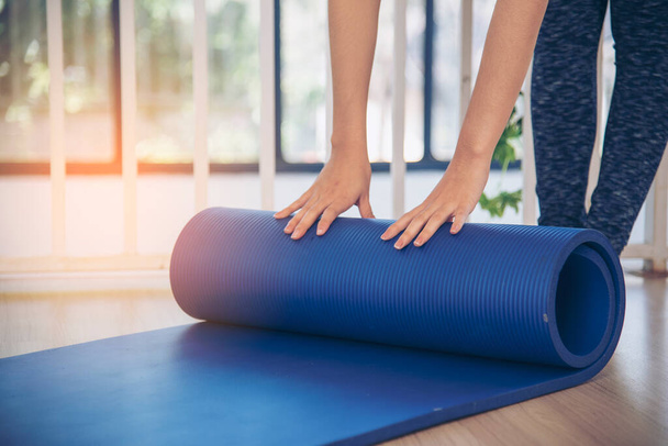 Woman hands rolled up yoga mat on gym floor in yoga fitness training room. Home workout woman close up hands rolling foam yoga gym mat. Woman barefoot home workout sportive healthy lifestyle concept - Foto, Imagem