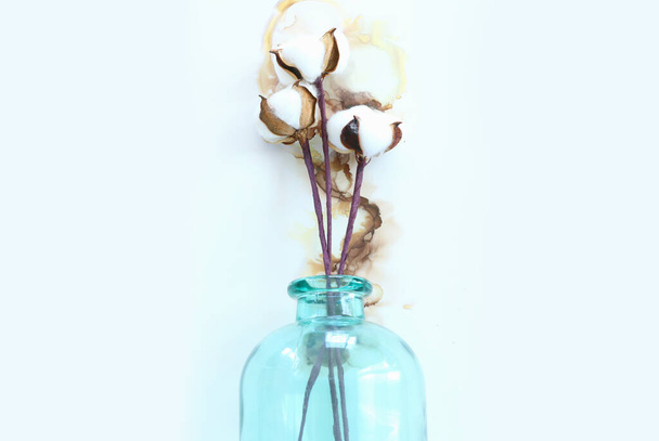 Sanatsal arkaplanda mavi cam vazodaki güzel pamuk çiçeklerinin yaratıcı görüntüsü. - Fotoğraf, Görsel