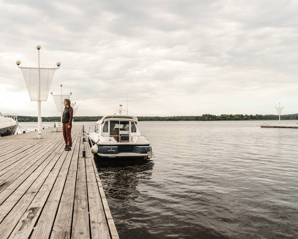 Горизонт река девушка в кожаной куртке и брюках осень ходить пирс лодка пирс ясное небо - Фото, изображение
