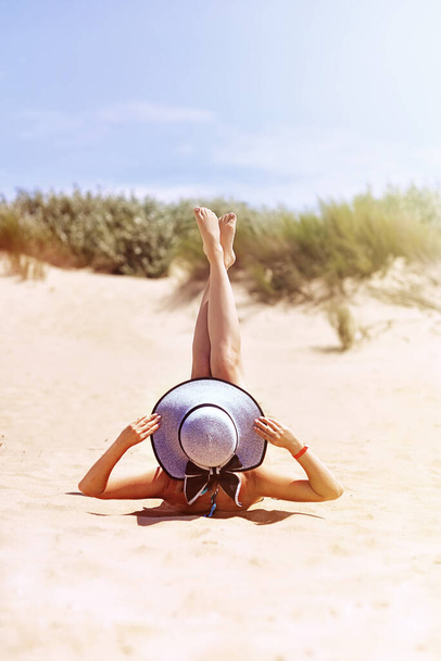 Zomer vakantie mode concept - zonnebadende vrouw met zonnehoed op het strand op het zand - Foto, afbeelding