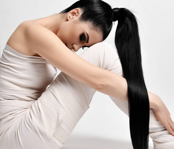 Side view of young brunette woman with ponytail hairstyle sitting in medical bandages on body, body wrap, looking down - Photo, Image