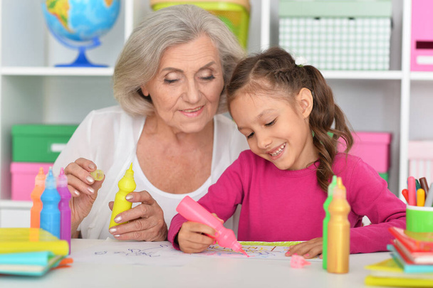 Portrait of a cute little girl drawing with her grandmother - Фото, изображение