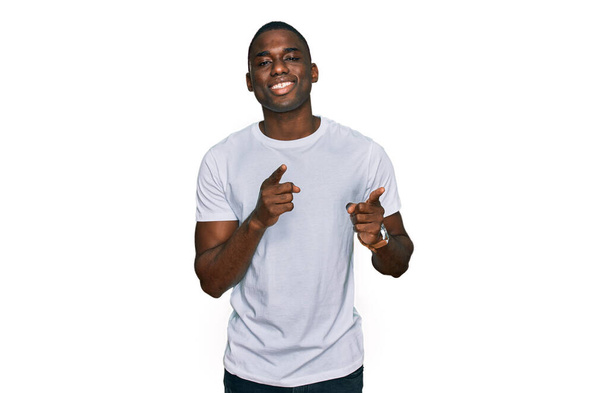 Gündelik beyaz tişört giyen genç Afro-Amerikan adam mutlu ve komik yüzlü parmaklarını kameraya doğrultuyor. iyi enerji ve titreşimler.  - Fotoğraf, Görsel