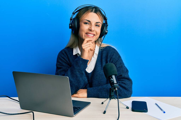 Giovane donna caucasica che lavora in studio radiofonico sorridente guardando fiducioso alla fotocamera con le braccia incrociate e mano sul mento. pensare positivo.  - Foto, immagini