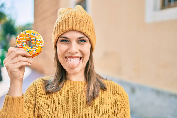 Jovem loira com língua fora segurando donut na cidade. - Foto, Imagem