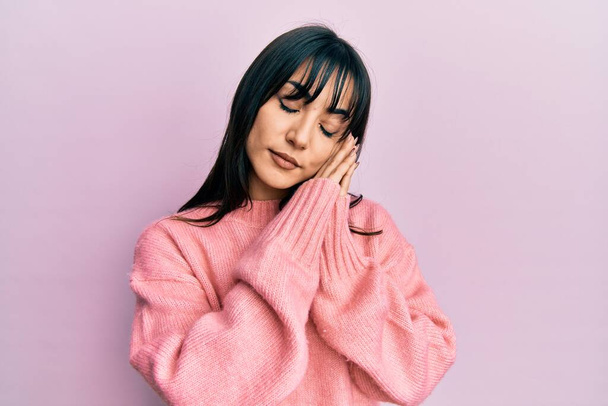 Young brunette woman with bangs wearing casual winter sweater sleeping tired dreaming and posing with hands together while smiling with closed eyes.  - Foto, afbeelding