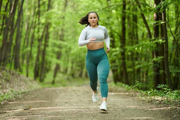 Beautiful plus size runner woman running on a dirt road in the forest - Photo, image