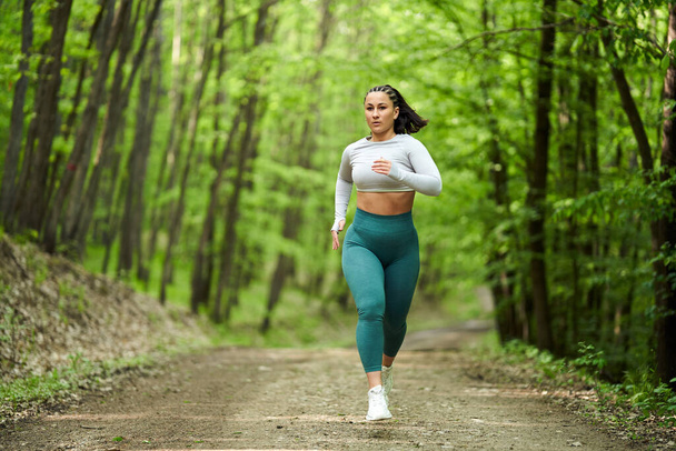 Beautiful plus size runner woman running on a dirt road in the forest - Foto, immagini
