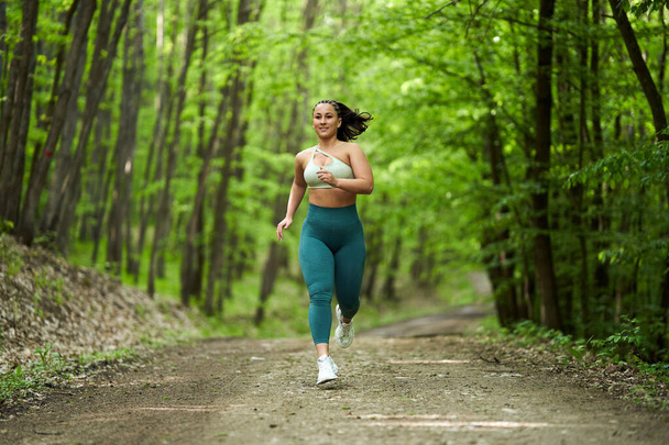 Hermosa mujer corredor de tamaño grande corriendo en un camino de tierra en el bosque - Foto, imagen