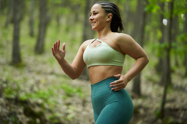 Beautiful plus size runner woman running on a dirt road in the forest - Photo, image