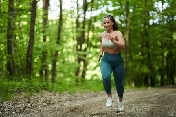 Beautiful plus size runner woman running on a dirt road in the forest - Foto, Bild