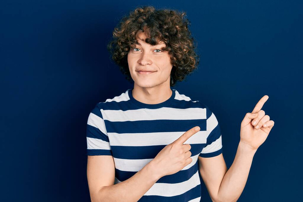 Handsome young man wearing casual striped t shirt smiling and looking at the camera pointing with two hands and fingers to the side.  - Photo, Image