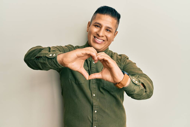 Young latin man wearing casual clothes smiling in love doing heart symbol shape with hands. romantic concept.  - Photo, Image