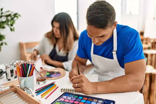 Dos estudiantes sonriendo feliz pintura sentados en la mesa en la escuela de arte. - Foto, imagen