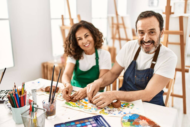 Двое школьников средних лет улыбаются счастливой модельной глине, сидя на столе в художественной школе. - Фото, изображение