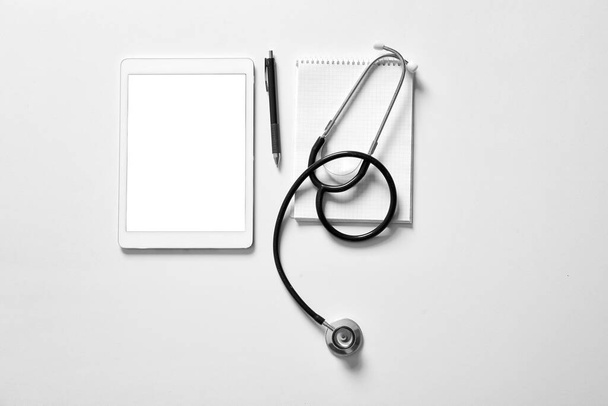Composition with modern stethoscope and tablet computer on light background - Foto, Imagem