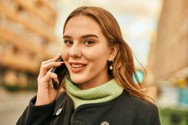 Fiatal szőke lány mosolyog boldog beszél az okostelefonon a városban. - Fotó, kép