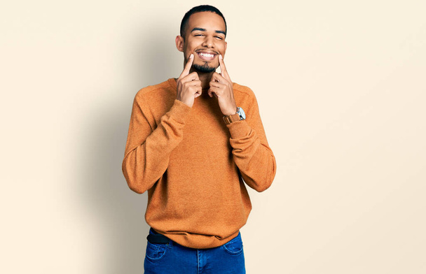 Young african american man wearing casual clothes smiling with open mouth, fingers pointing and forcing cheerful smile  - Fotó, kép