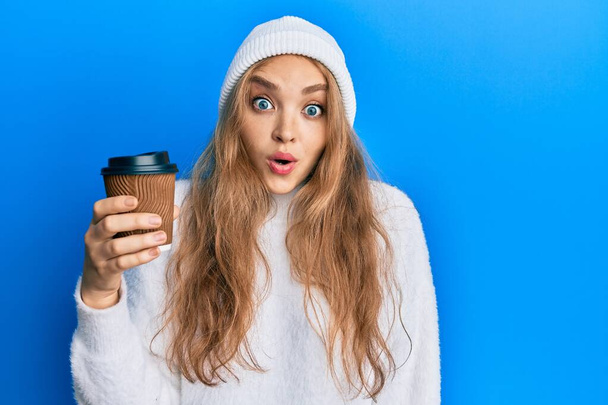 Belle femme caucasienne blonde buvant une tasse de café à emporter effrayée et étonnée avec la bouche ouverte pour la surprise, visage incrédule  - Photo, image