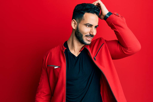 Young hispanic man wearing red leather jacket smiling confident touching hair with hand up gesture, posing attractive and fashionable  - Фото, изображение