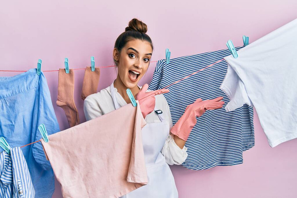 Beautiful brunette young woman washing clothes at clothesline amazed and smiling to the camera while presenting with hand and pointing with finger.  - 写真・画像
