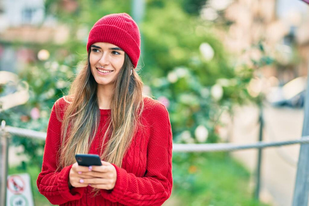 Молодая латиноамериканка в зимнем стиле с помощью смартфона в городе. - Фото, изображение