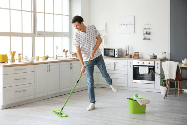 Young man mopping floor in kitchen - Фото, изображение