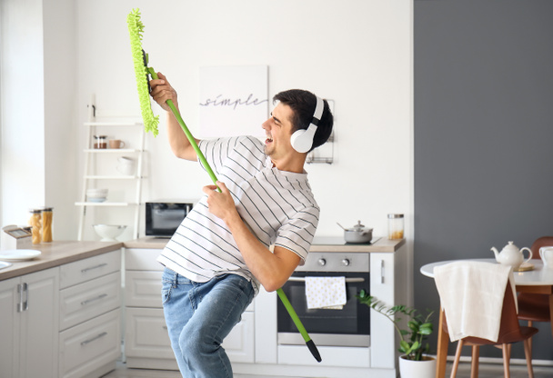 Young man mopping floor while listening to music in kitchen - Foto, Imagen