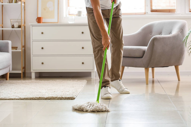 Young man mopping floor in living room - Foto, immagini