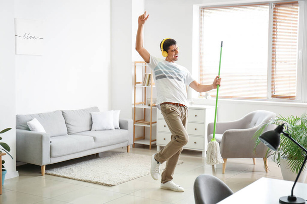 Young man listening to music while mopping floor in living room - Foto, immagini