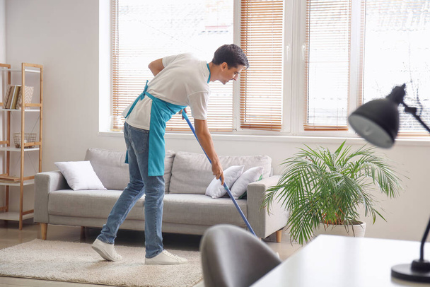Young man mopping floor in living room - Foto, imagen