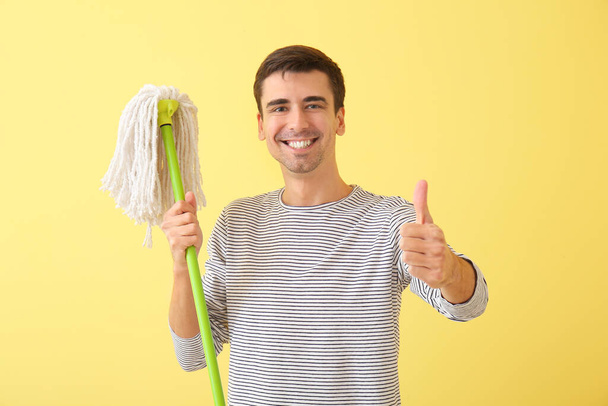 Young man with floor mop showing thumb-up on color background - Fotó, kép