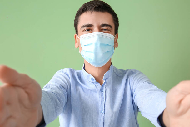 Joven hombre en brazos de apertura máscara médica para abrazo sobre fondo de color - Foto, Imagen