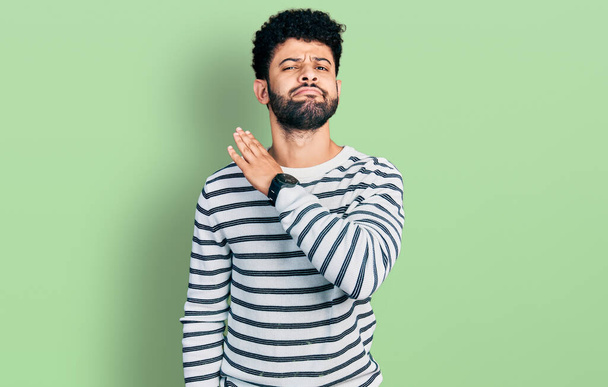 Young arab man with beard wearing casual striped sweater cutting throat with hand as knife, threaten aggression with furious violence  - Fotoğraf, Görsel