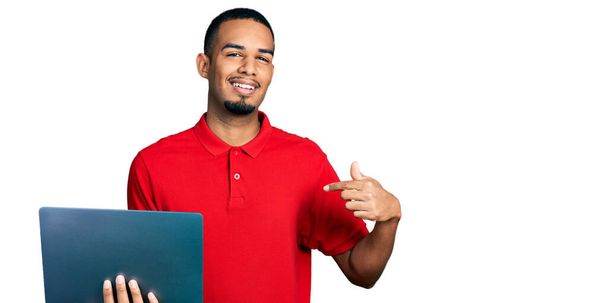 Genç Afro-Amerikalı bir adam bilgisayarla çalışıyor. Kendini mutlu ve gururlu bir şekilde gösteren birini işaret ediyor.  - Fotoğraf, Görsel
