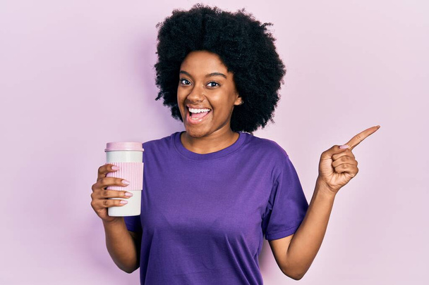 Giovane donna afroamericana che tiene il caffè sorridente felice indicando con mano e dito di lato  - Foto, immagini