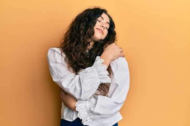 Young brunette woman with curly hair wearing casual clothes hugging oneself happy and positive, smiling confident. self love and self care  - Fotografie, Obrázek