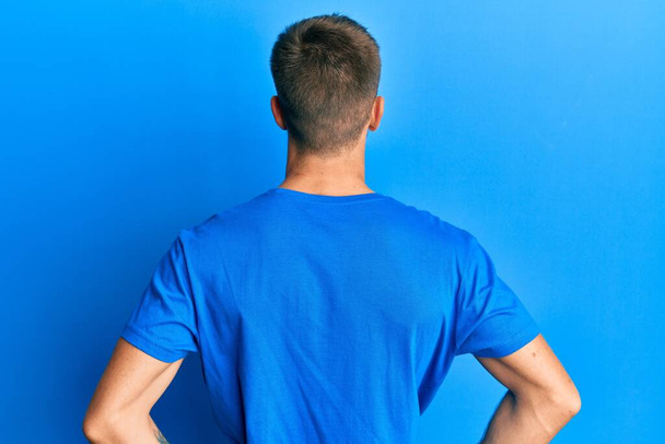 Nuori valkoihoinen mies päällään rento sininen t-paita seisoo taaksepäin katsoen pois kädet vartalossa  - Valokuva, kuva