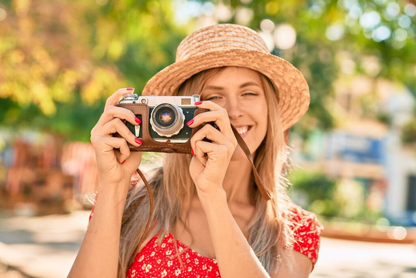 Young blonde tourist woman wearing summer style using vintage camera at the park - Photo, Image