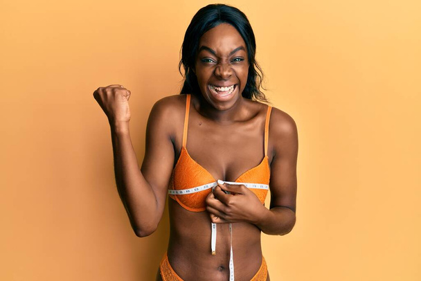若いアフリカ系アメリカ人の女性は、テープメジャーを使用してランジェリーを身に着けていることは誇りに叫びます,勝利と成功を祝います非常に腕を上げ  - 写真・画像