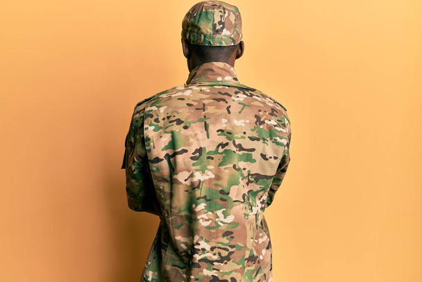 Giovane uomo afroamericano indossando uniforme dell'esercito in piedi all'indietro guardando lontano con le braccia incrociate  - Foto, immagini