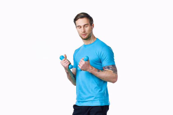 guy with dumbbells go in for sports in a blue t-shirt on a light background - Photo, Image
