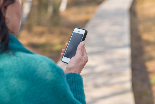 Une femme détient un téléphone intelligent cellulaire avec écran vide, vue arrière sur le paysage forestier printanier. - Photo, image