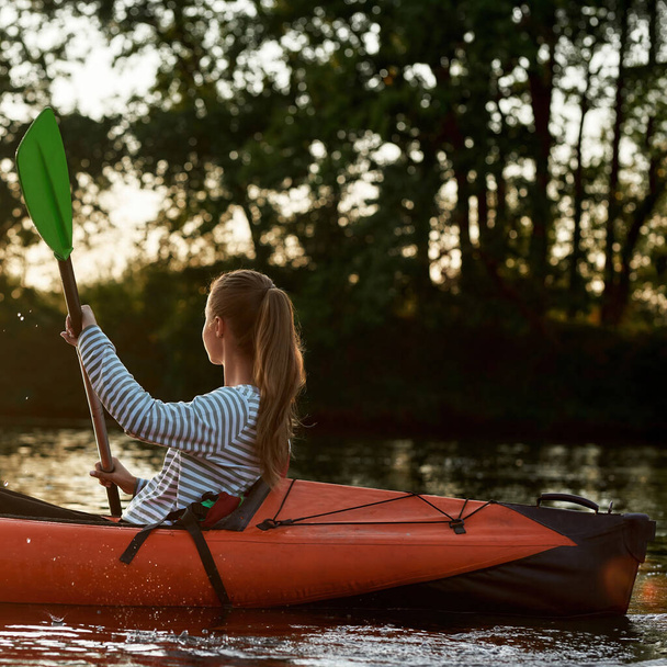 Relaxed young woman looking away while kayaking in a lake surrounded by nature on a late summer afternoon - Photo, Image