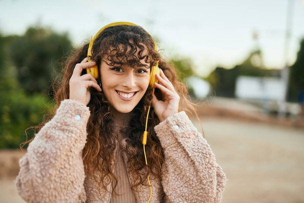 Joven mujer hispana sonriendo feliz usando auriculares en la ciudad - Foto, Imagen