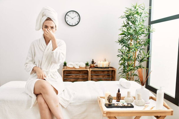 Young blonde woman wearing bathrobe at wellbeing spa tired rubbing nose and eyes feeling fatigue and headache. stress and frustration concept.  - Valokuva, kuva